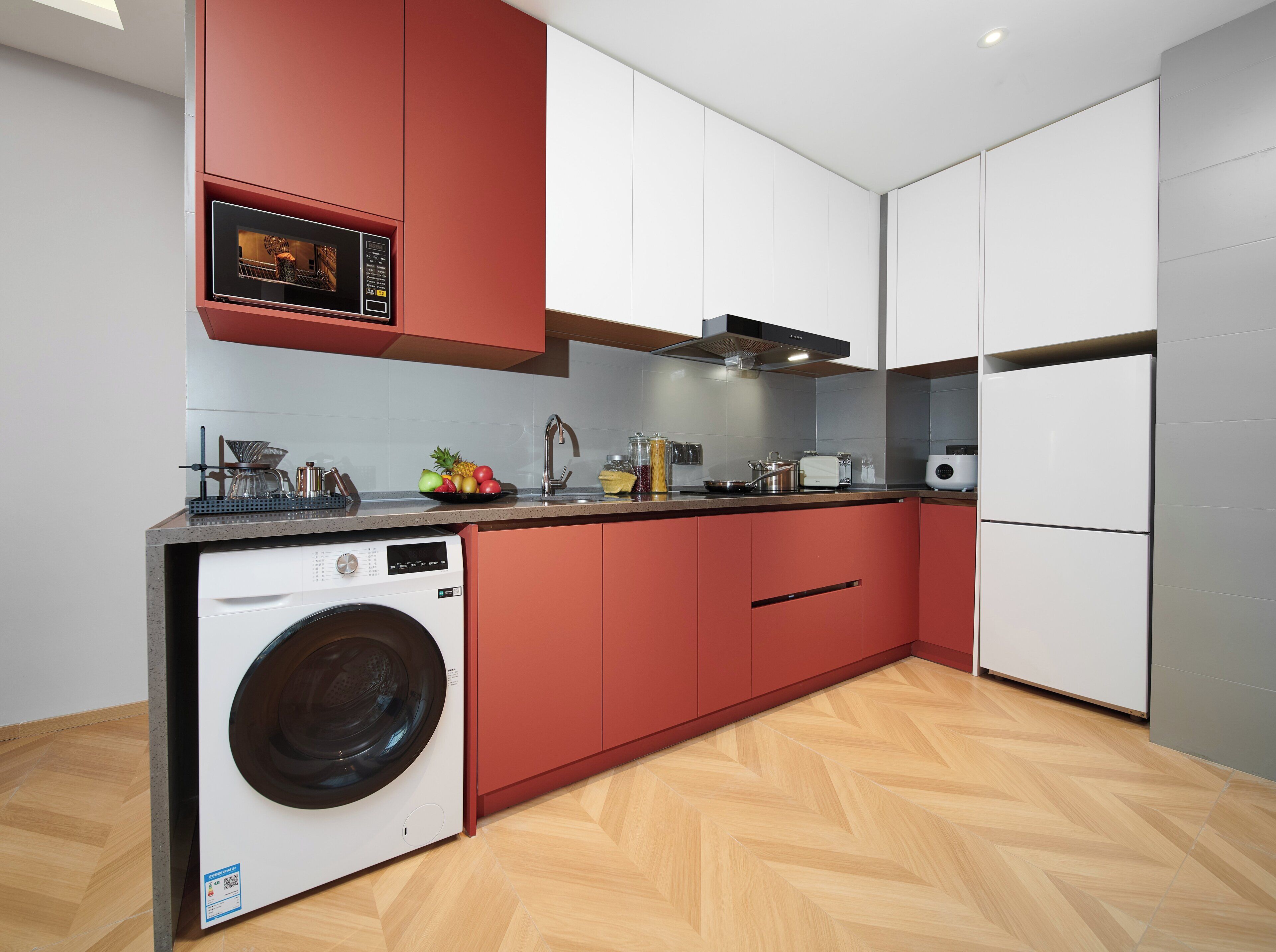 A modern kitchen with red cabinetry, a built-in washing machine, and a stainless steel sink.