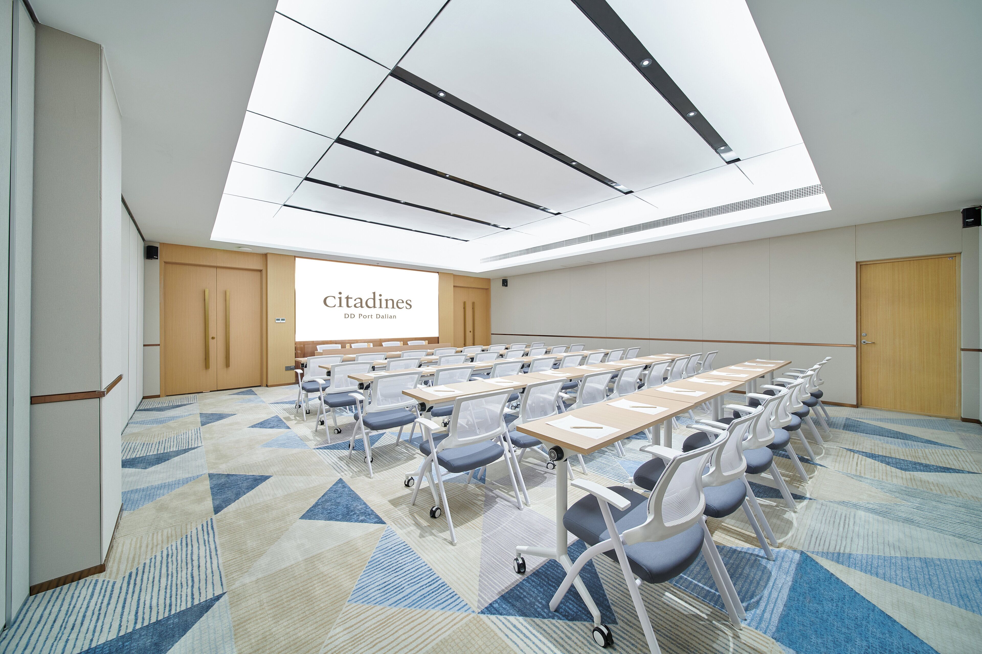 Un salón de conferencias con techo alto, una pantalla grande y filas de sillas y mesas.
