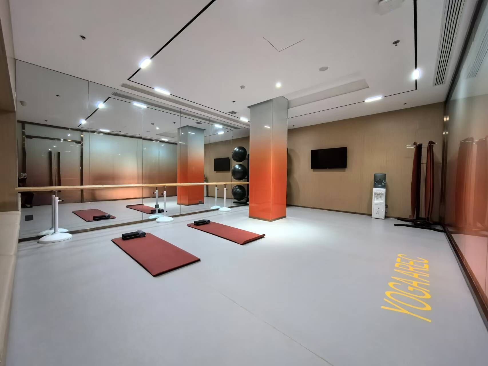 A modern yoga studio with mirrored walls, a central pillar, and a yoga mat area.