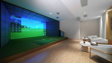 Une pièce moderne dotée d’un grand écran diffusant un match de golf, d’un petit espace vert et d’un coin salon avec des chaises blanches et une table.