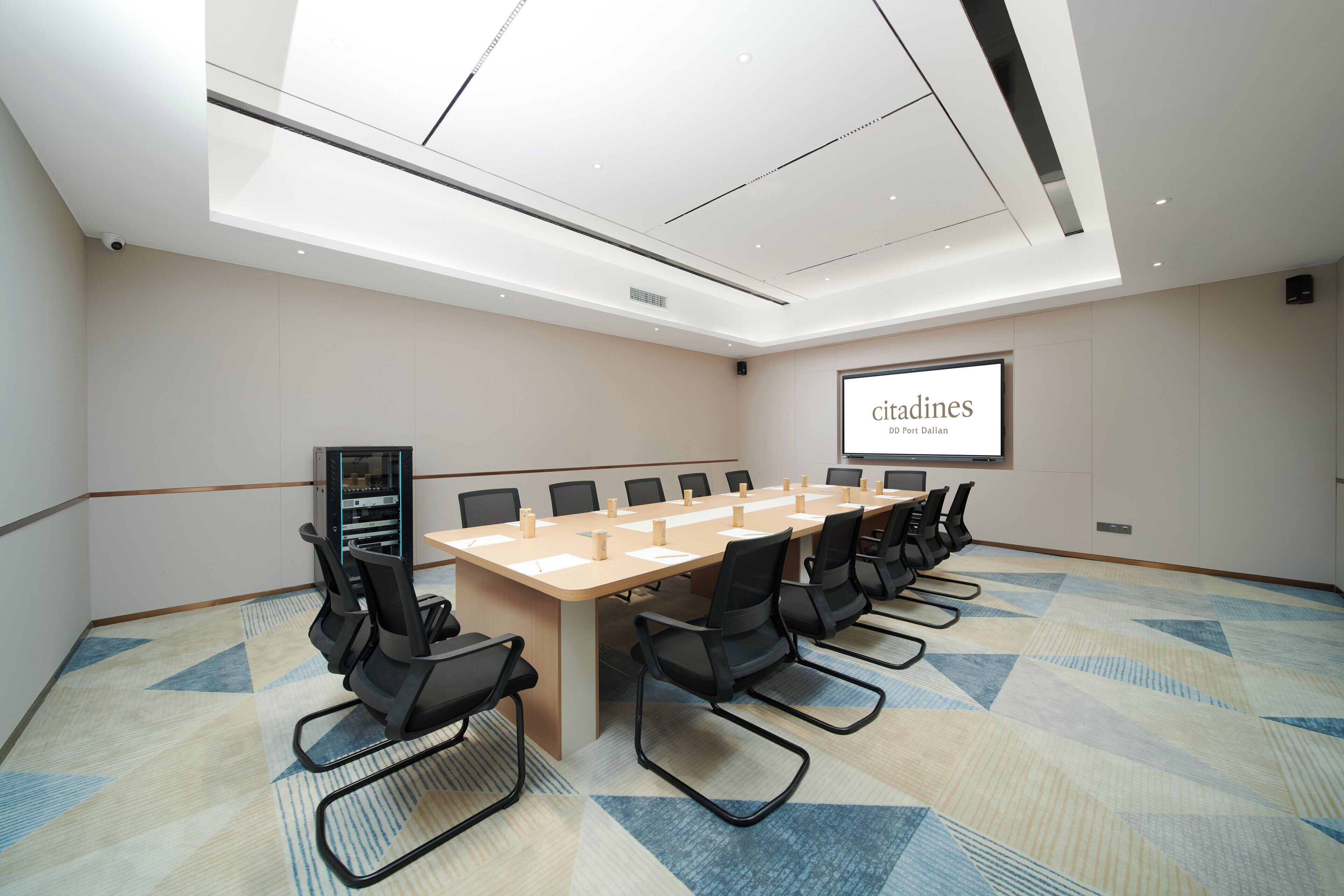 A conference room with a long table, multiple chairs, a projector screen, and a carpeted floor.