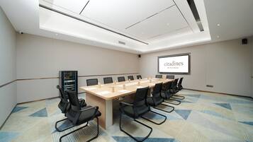 A conference room with a long table, multiple chairs, a projector screen, and a carpeted floor.