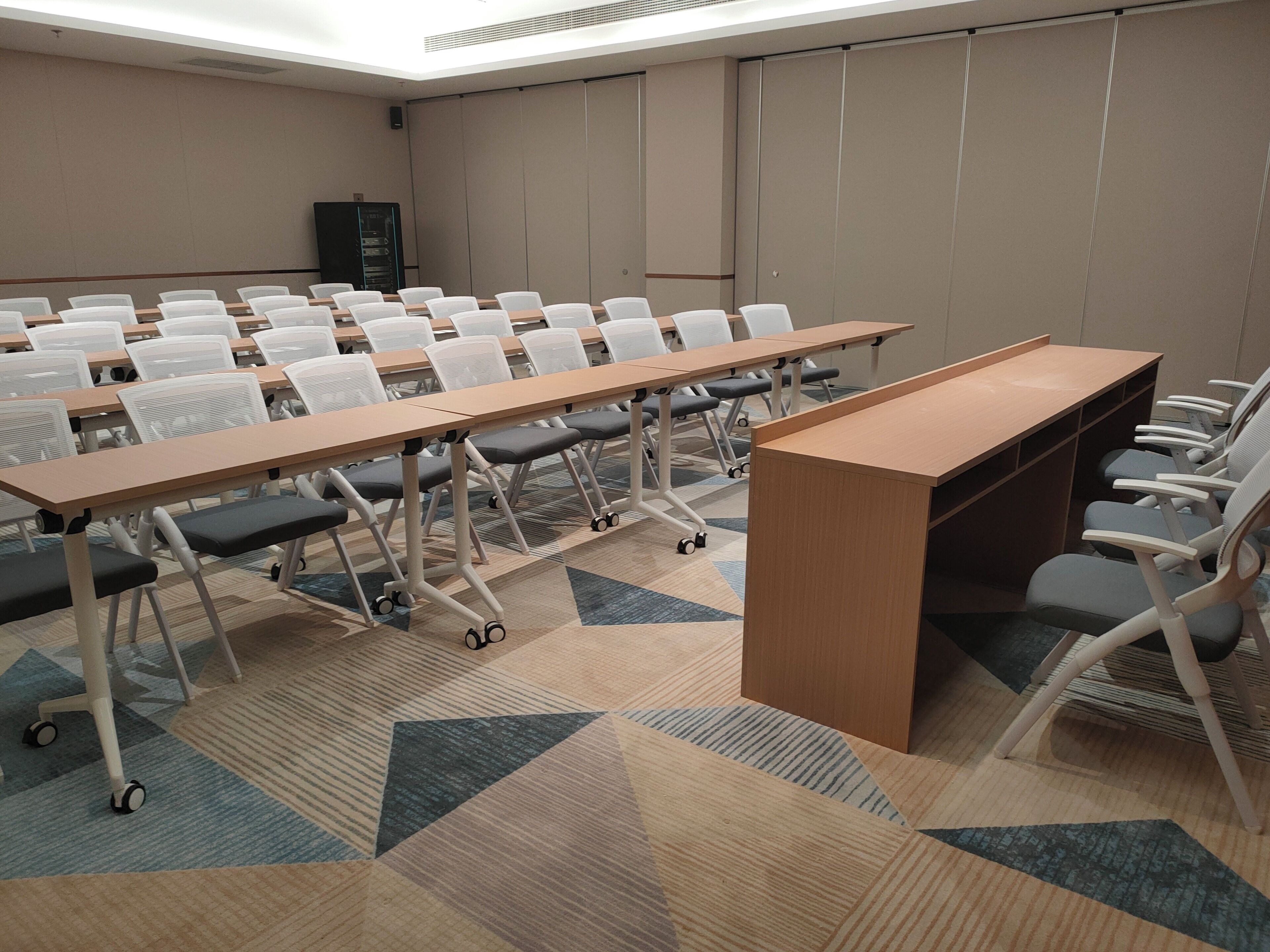 A conference room with rows of chairs and tables, a podium, and a carpeted floor.
