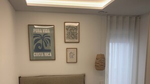 En snyggt bäddad säng med ett turkosfärgat överkast och kuddar, en inramad bild av en palm och ett inramat citat på väggen.
