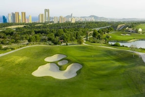 A golf course with bunkers, a water hazard, and a city skyline in the background. - Campana Bay Villa (Finestrat)