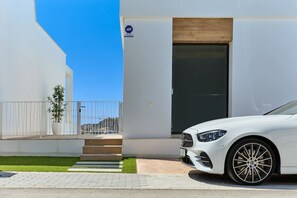 A white car parked in front of a modern building with a large door and a small window.