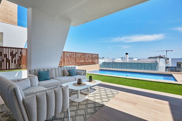 A modern outdoor living area with a pool, a sofa set, and a coffee table.