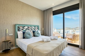 Habitación de hotel moderna con una cama grande, vistas a la ciudad y un balcón con una silla de mimbre.