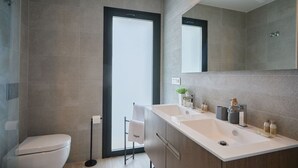 A modern bathroom with a toilet, a shower, and a vanity with a sink and mirror. - Campana Bay Villa (Finestrat)