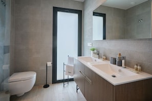 A modern bathroom with a toilet, a shower, and a vanity with a sink and mirror. - Campana Bay Villa (Finestrat)