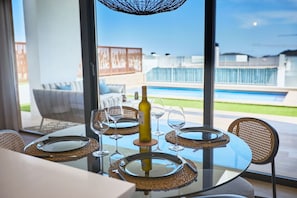 A dining table set for four with wine glasses and a bottle, overlooking a swimming pool and outdoor seating area. - Campana Bay Villa (Finestrat)