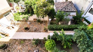 Un cortile con tetto in tegole, piante in vaso, una statua e un vialetto in pietra.