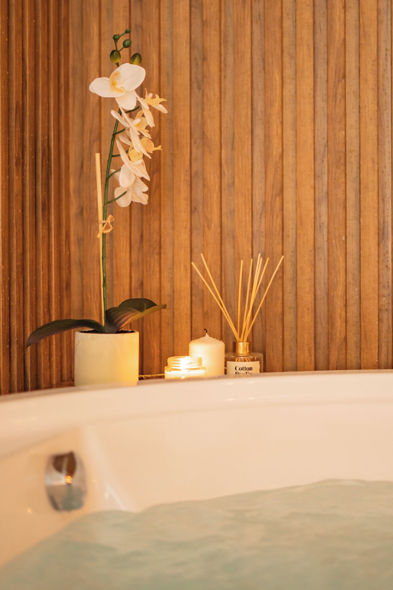 A spa setting with a wooden wall, a potted orchid, candles, and reed diffusers.