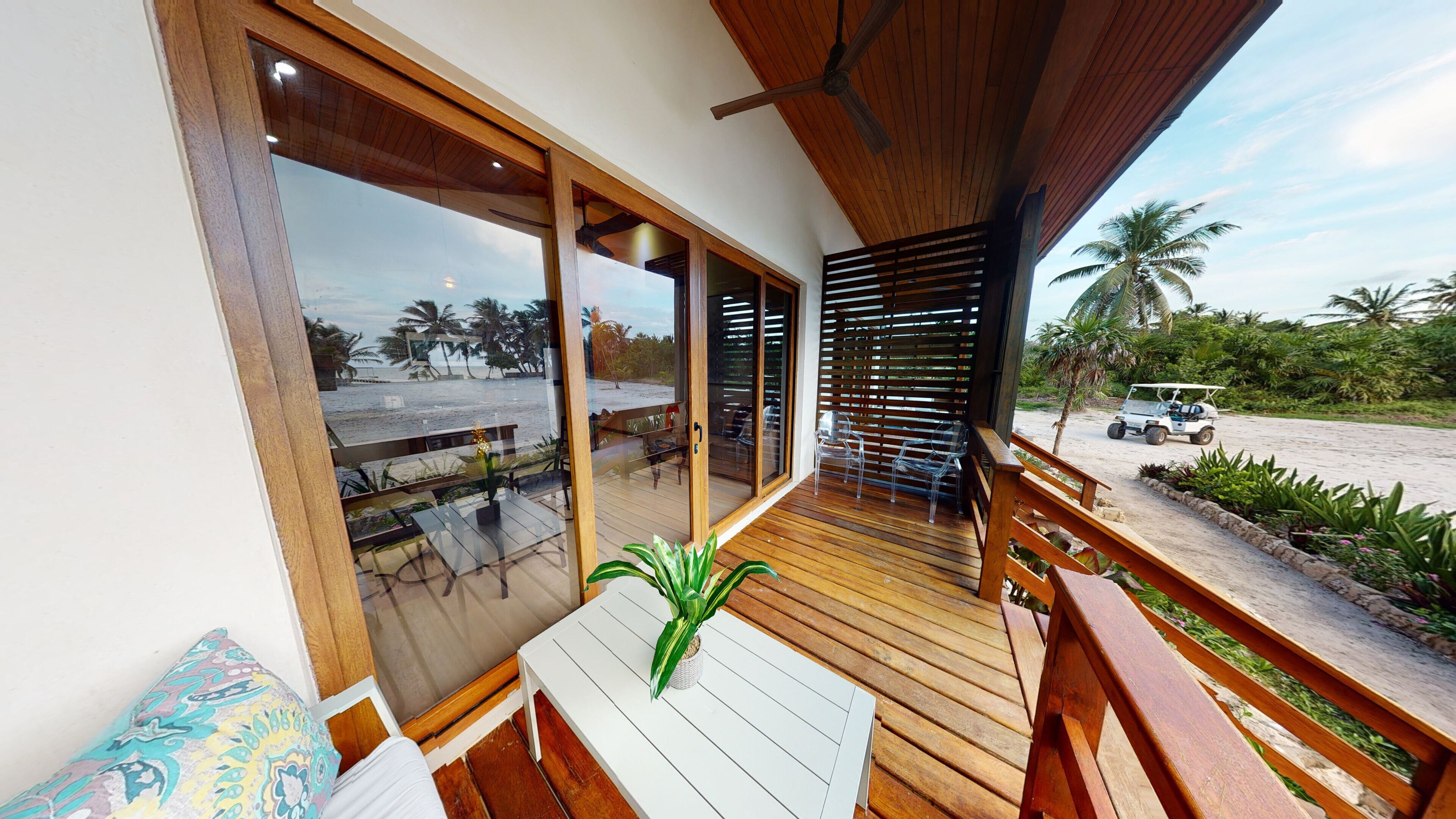 A wooden deck with a glass door leading to a beach view, a table with chairs, and a small potted plant.
