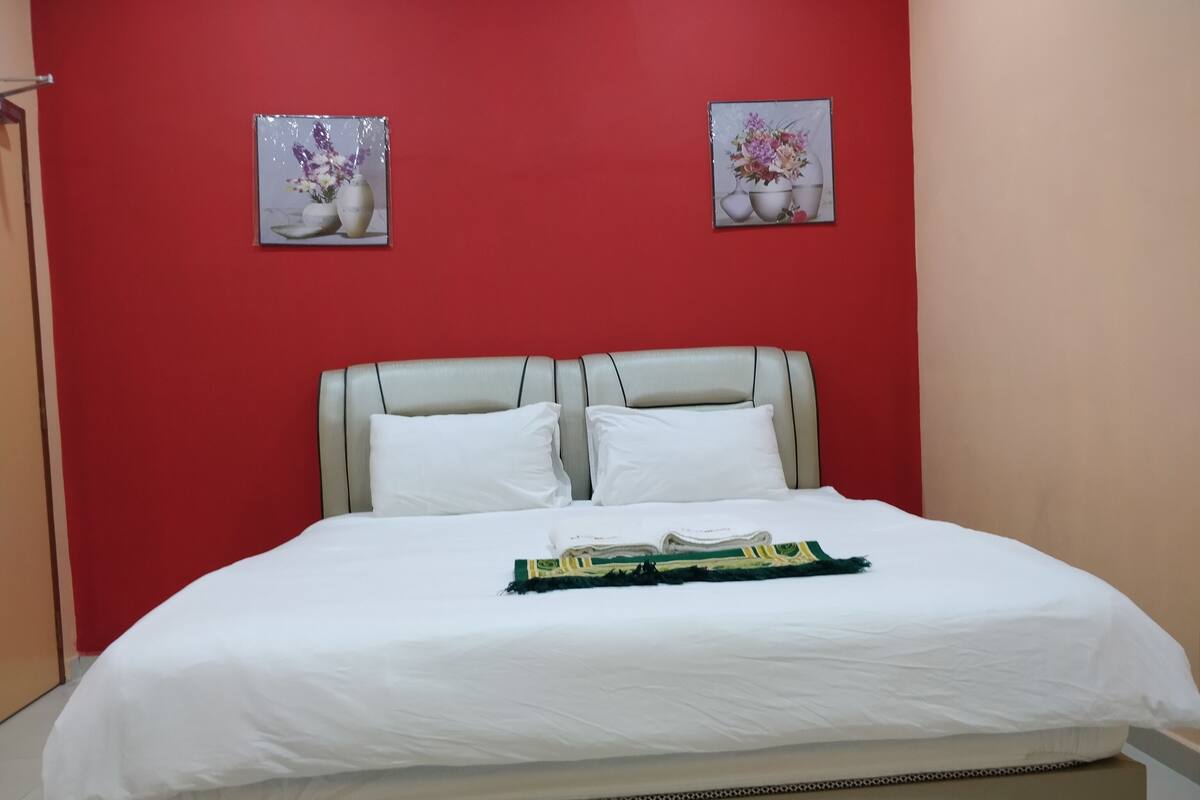 A bed with white bedding, a beige headboard, and two framed floral pictures on a red wall.