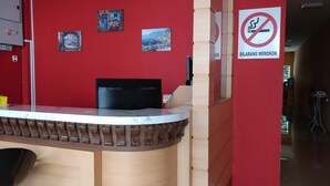 A reception desk with a black monitor, a no-smoking sign, and a red wall with framed pictures. - Hotel O Puteri Miqaila (Bota)