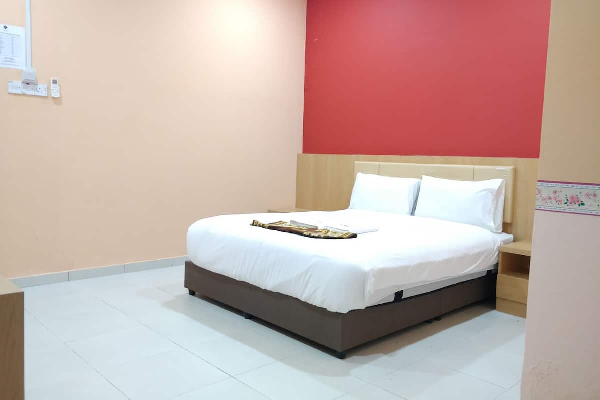 A neatly made bed in a room with a red accent wall, white bedding, and a small bedside table.