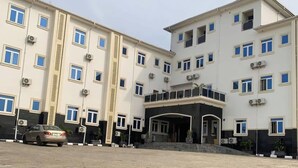 A multi-story hotel with a central entrance, a paved courtyard, and a parked car. - AJ'S Hotel & Suites (Abuja)