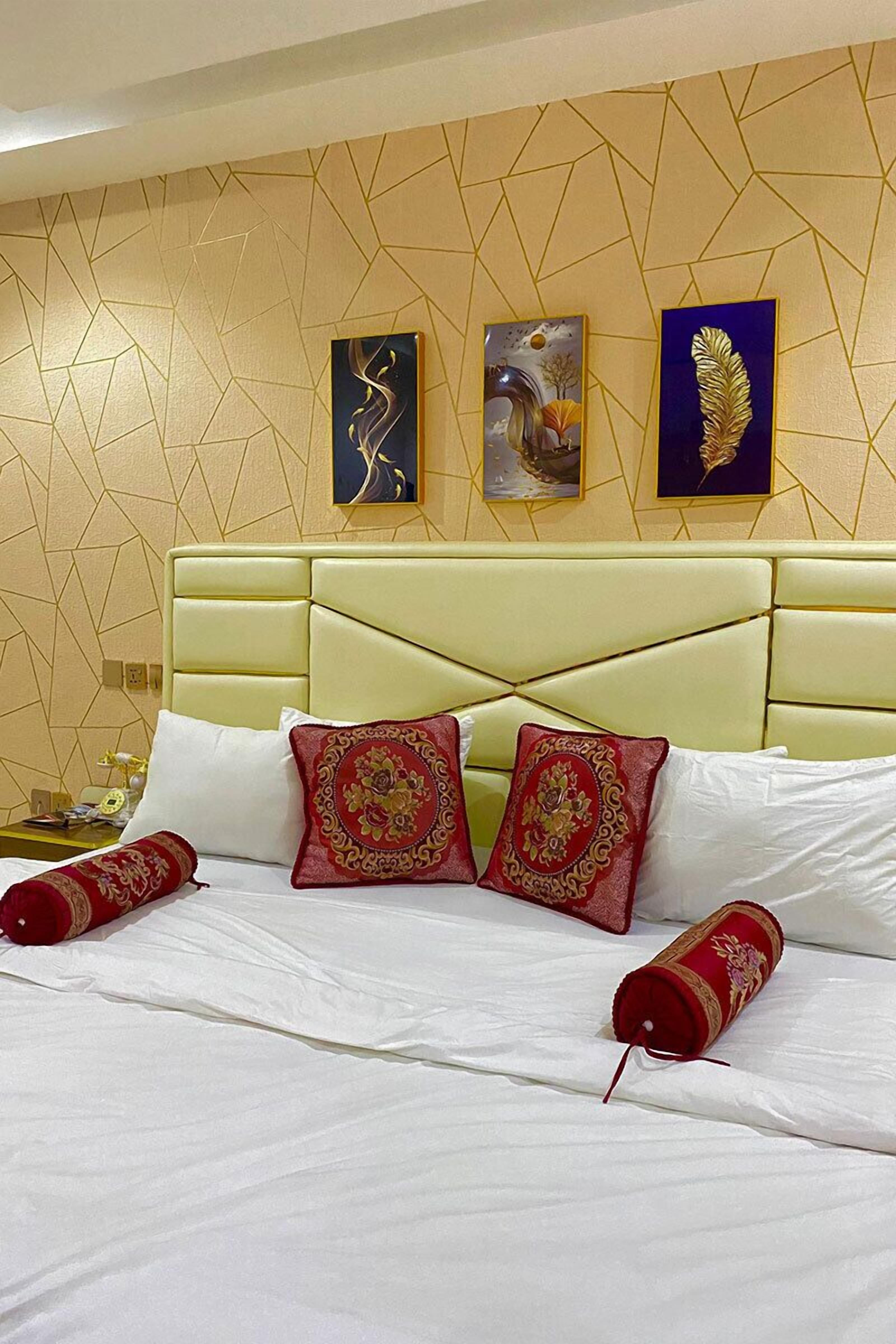 A hotel room with a geometric-patterned wall, a cream-colored headboard, and three artworks above the bed.