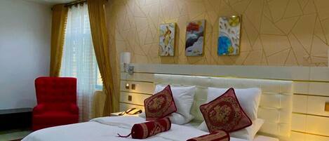 A hotel room with a bed, a red armchair, a bedside table, and an air conditioning unit.