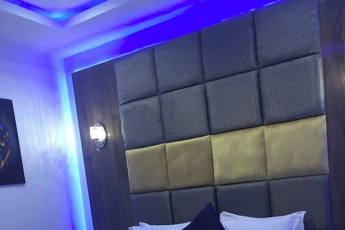 Une chambre d’hôtel moderne avec un grand lit, une tête de lit rembourrée et une lampe fixée au mur.