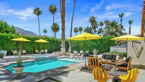 A pool area with yellow umbrellas, lounge chairs, and a wooden sofa set. - Good Vibes Only – Historic Spanish Hacienda with Pool, Spa, Fire Pit & Mountain Views (Palm Springs)