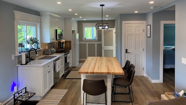 A modern kitchen with white cabinets, a wooden dining table, and a built-in oven.