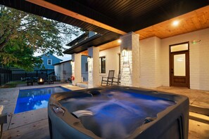 Un bain à remous avec une terrasse en bois, une piscine et un mur en briques doté d’une porte.