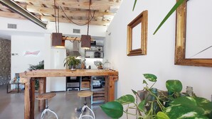 A kitchen with a wooden table, bar stools, hanging lights, and potted plants.