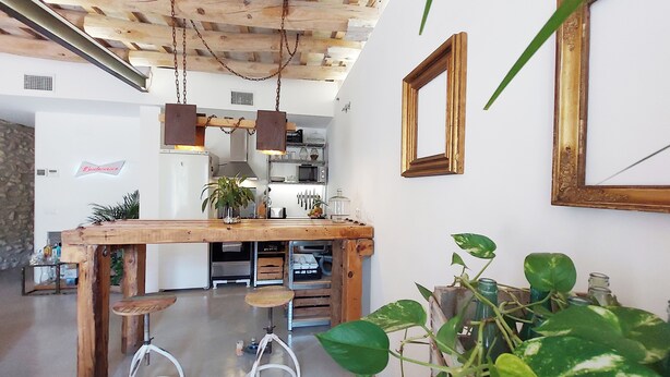 A kitchen with a wooden table, bar stools, hanging lights, and potted plants.