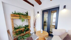 A cozy room with a wooden plant wall, a round wooden table, a small stool, and a sofa.