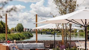 Eine Uferterrasse mit Sitzgelegenheiten, Sonnenschirmen und einer Steinmauer.