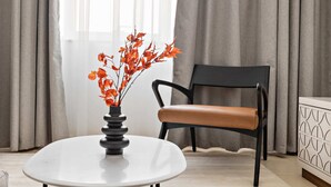 A modern room with a round white table, a black chair with brown cushions, and a decorative vase with orange flowers. - Silkhaus Art Residence Sheikh Zayed Road (Dubai)