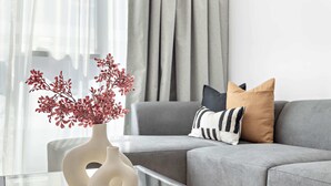 A modern living room with a grey sofa, a glass coffee table, and decorative vases with red branches. - Silkhaus Art Residence Sheikh Zayed Road (Dubai)