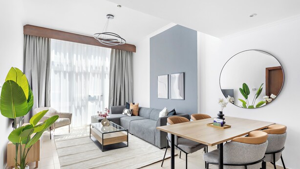 A modern living room with a grey sofa, a wooden dining table with chairs, a coffee table, and a large mirror on the wall. - Silkhaus Art Residence Sheikh Zayed Road (Dubai)