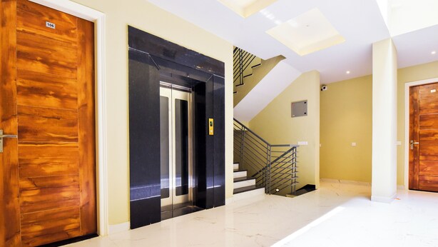 Un intérieur moderne avec un sol en marbre, des portes en bois, un ascenseur noir et un escalier.