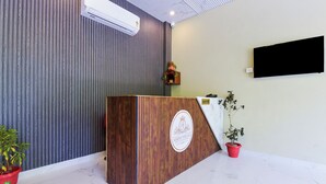 Un comptoir d’accueil avec un revêtement en bois et un logo, un climatiseur fixé au mur, un téléviseur à écran plat et des plantes en pot.
