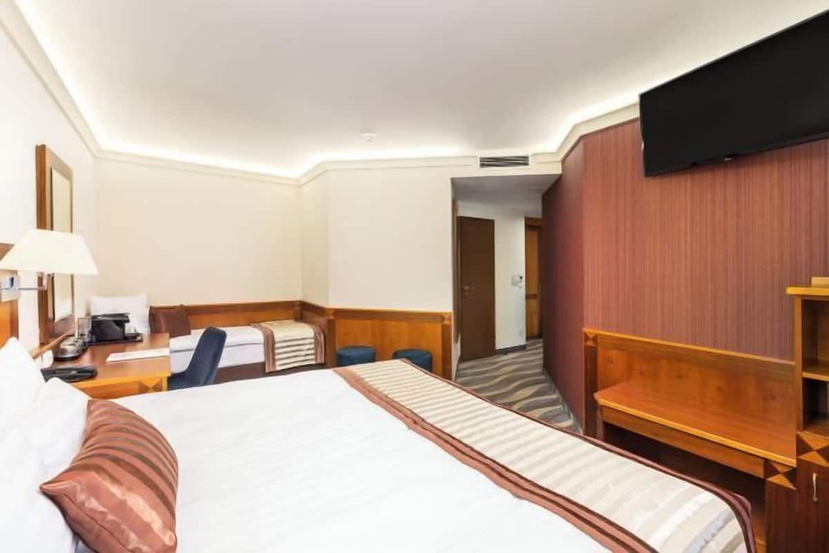 Ein Hotelzimmer mit Bett, Schreibtisch mit Lampe, Stuhl und Wandfernseher.