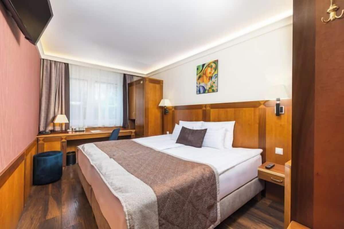 Ein Hotelzimmer mit einem Bett, Nachttischen, einem Schreibtisch, einem Sessel, einer Lampe und einem Bild an der Wand.