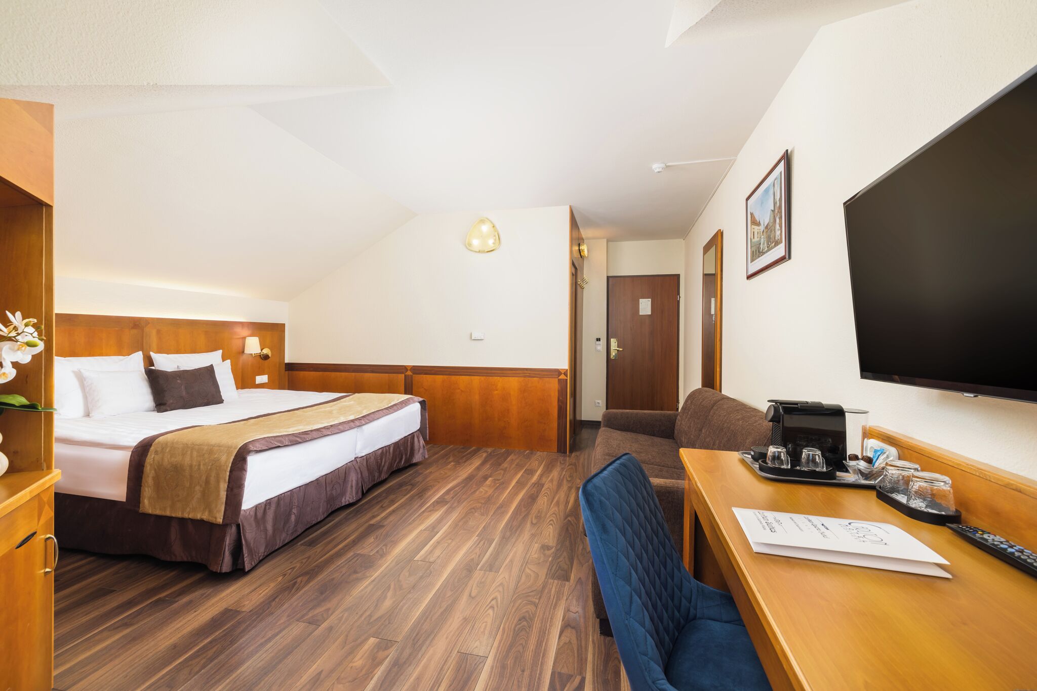 A hotel room with a bed, a desk with a chair, a television, and a door.