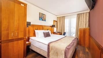 Een hotelkamer met een groot bed, een houten garderobe, nachtkastje, lamp en een aan de muur bevestigde televisie.