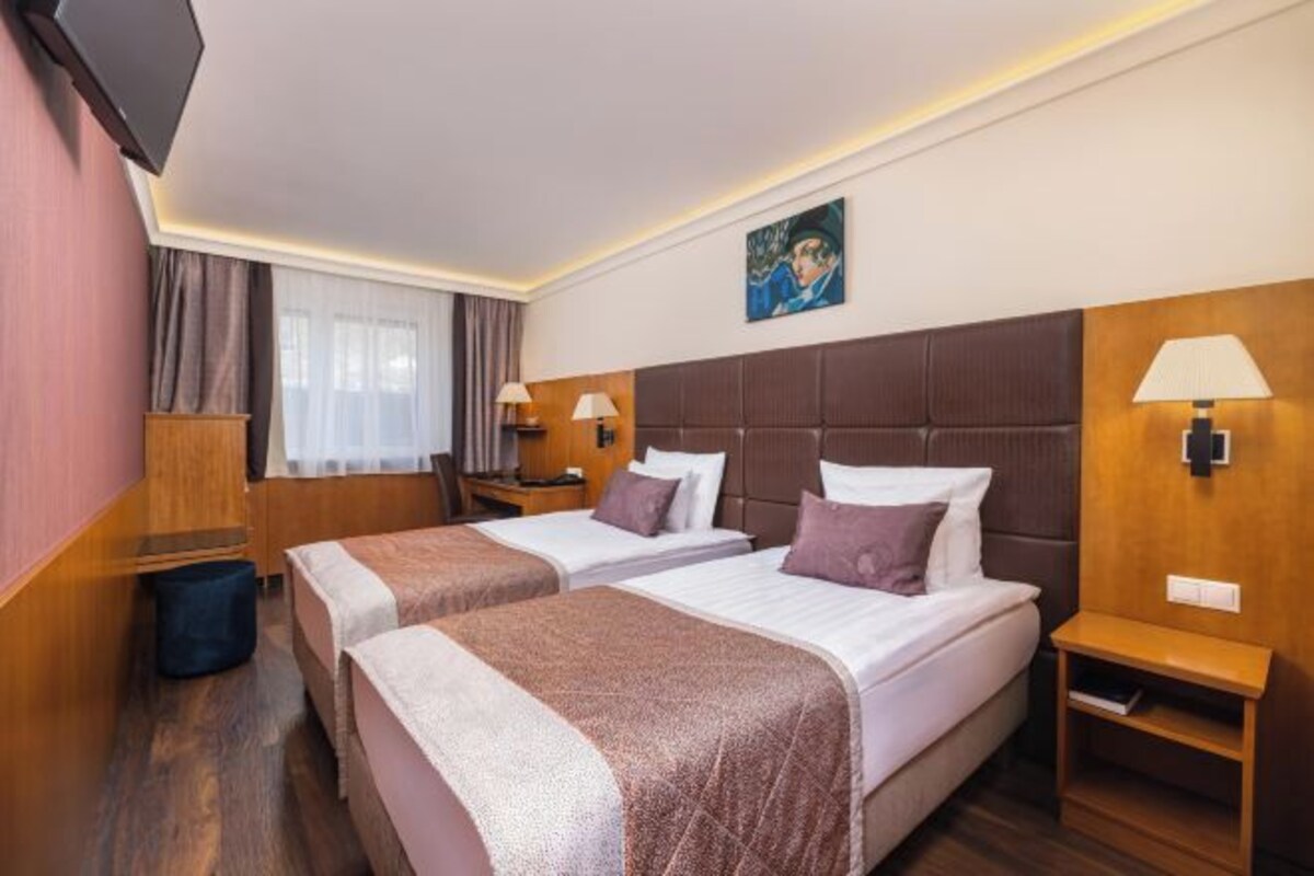 A hotel room with two beds, a TV, bedside lamps, a painting, and a wooden nightstand.