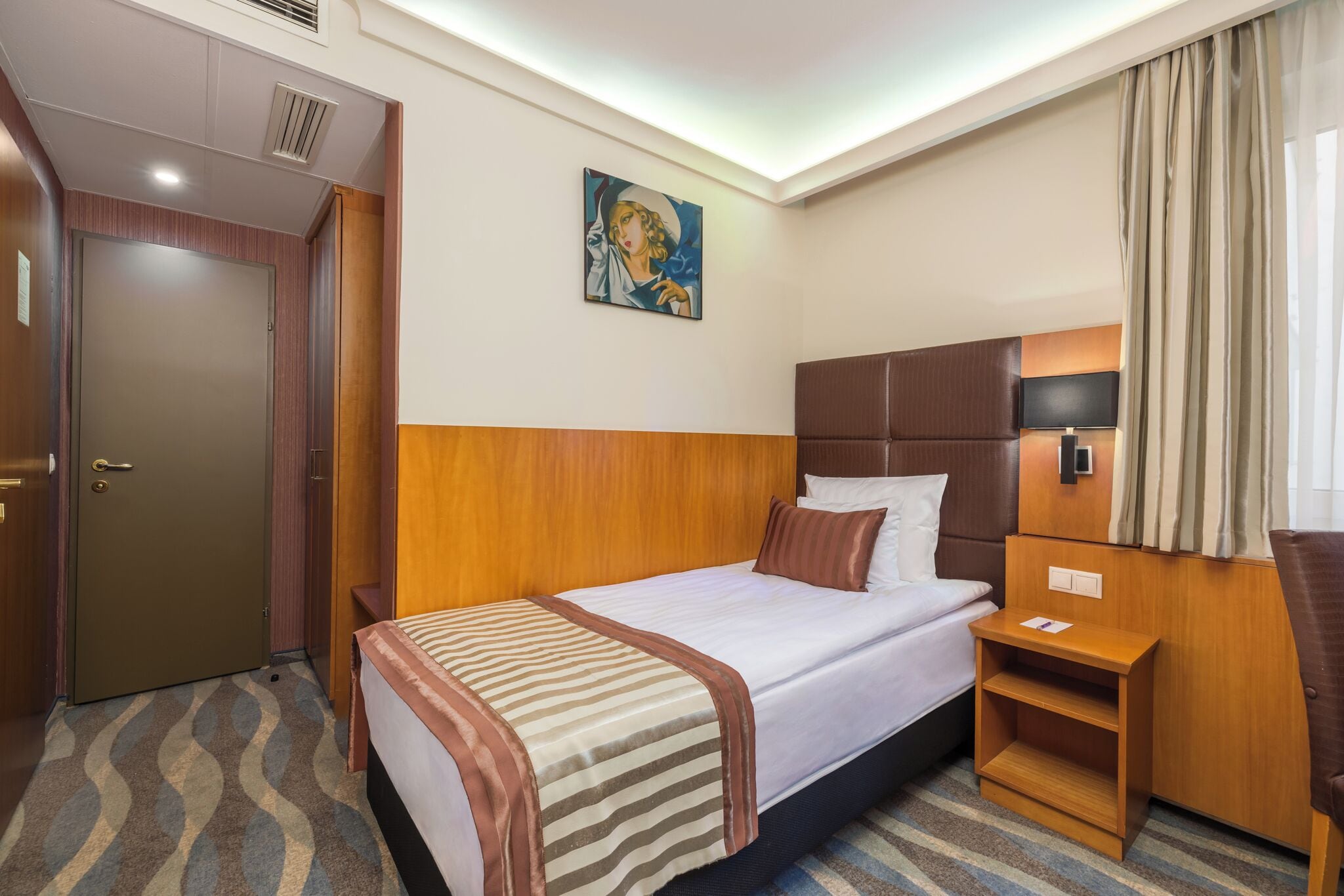 Una habitación de hotel con cama, mesita de noche y un cuadro en la pared.