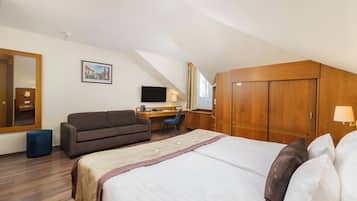 Habitación de hotel con cama, escritorio, silla, sofá, armario y televisor.