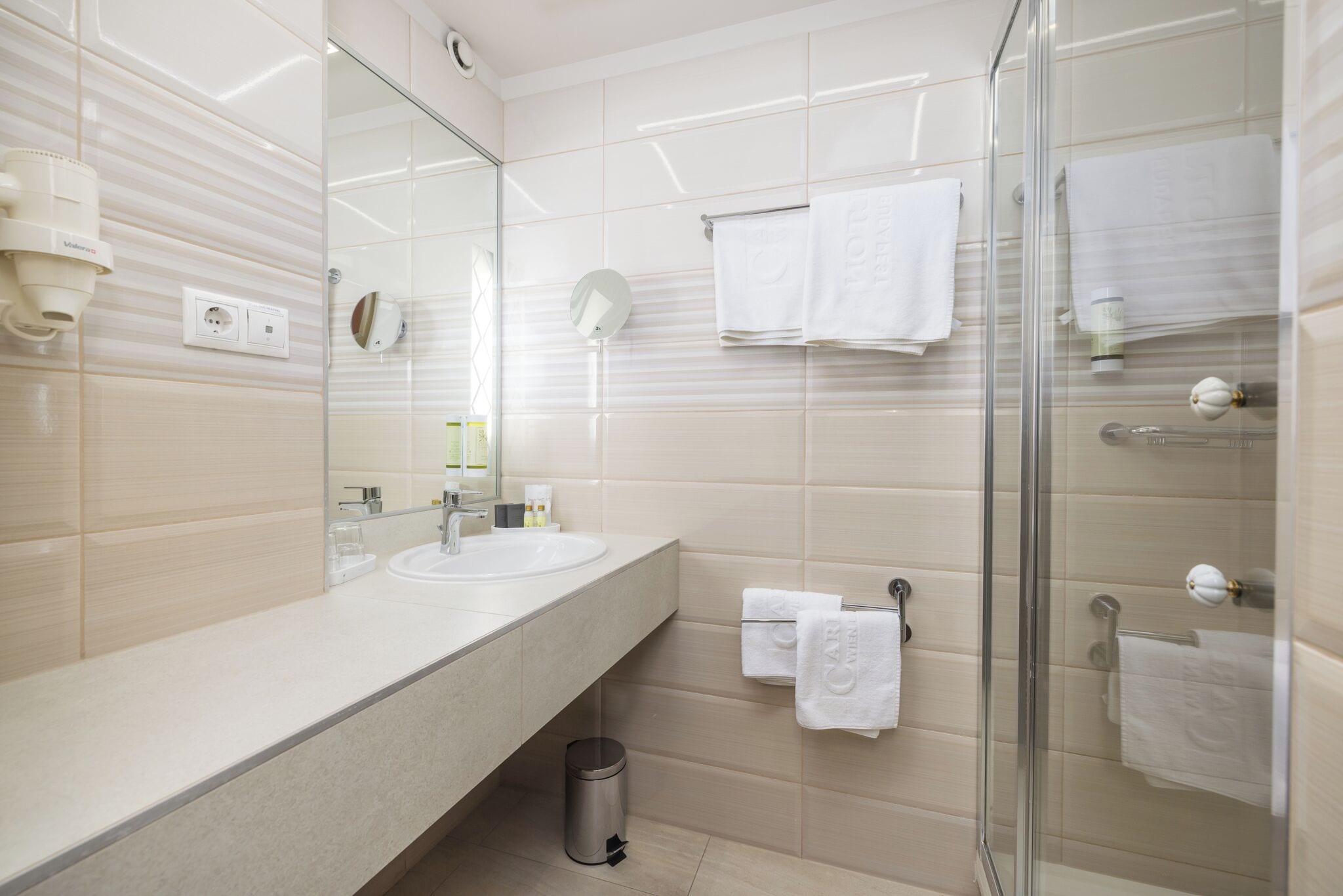 A modern bathroom with a large mirror, two sinks, a glass shower enclosure, and neatly arranged towels.