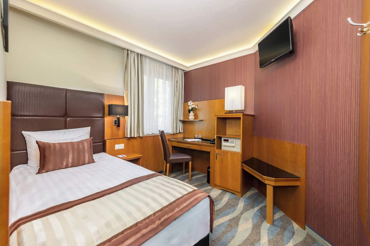 Ein Hotelzimmer mit einem großen Bett, einem Schreibtisch, einem Stuhl, einem Fernseher und einem kleinen Schrank.