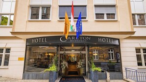 La entrada del Hotel Carlton de Budapest, con banderas, fachada de vidrio y un acceso acogedor.