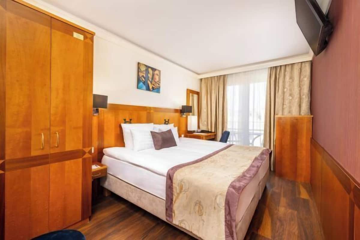 Ein Hotelzimmer mit einem großen Bett, einem Holzschrank, einem Nachttisch, einer Lampe und einem an der Wand befestigten Fernseher.