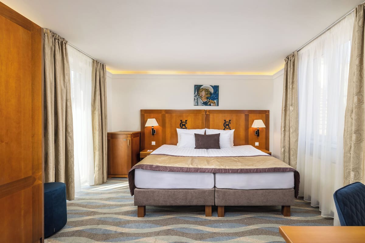 Ein Hotelzimmer mit einem großen Bett, einem hölzernen Kopfteil, zwei Nachttischlampen, einer kleinen Kommode und einem Bild an der Wand.