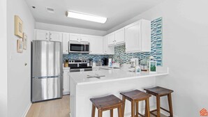 A modern kitchen with white cabinets, stainless steel appliances, a tiled backsplash, and a central island with stools.